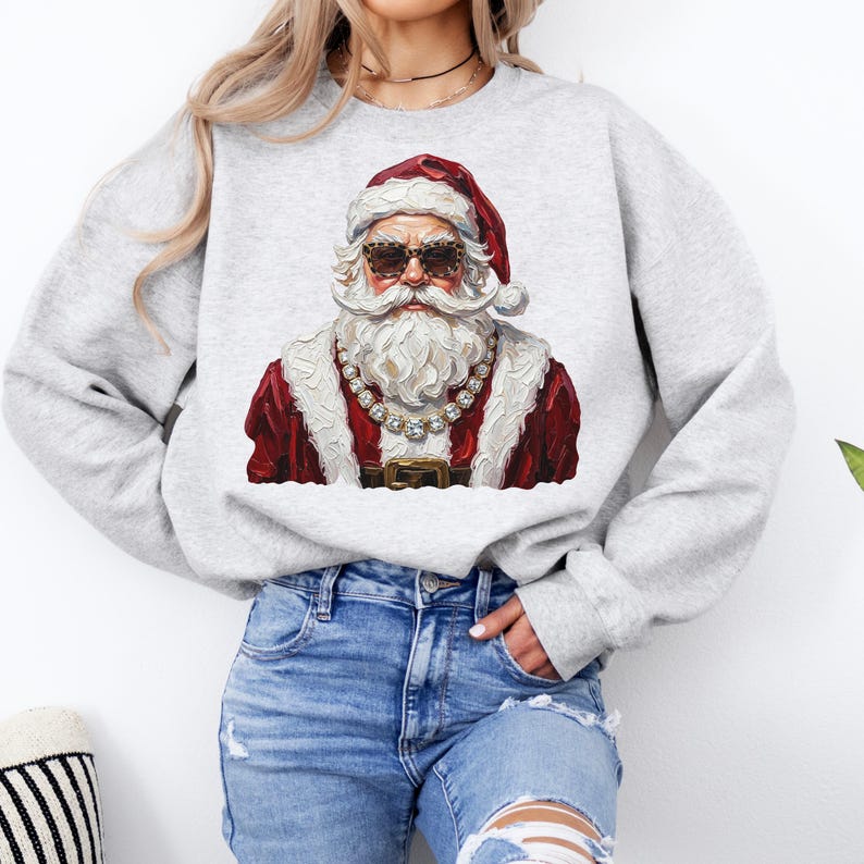 May include: A light gray crewneck sweatshirt featuring a graphic print of Santa Claus wearing leopard print sunglasses and a large crystal-style chain necklace. The design depicts Santa in a red coat with white fur trim and a matching red hat.