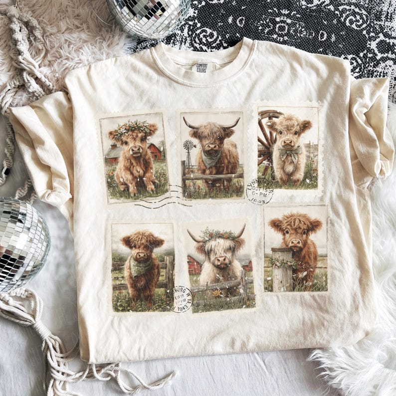 May include: Cream-colored t-shirt featuring six rectangular images of Highland cows. Each image showcases a different cow with floral accents, set against a rural backdrop. The shirt has a classic crew neck and short sleeves.