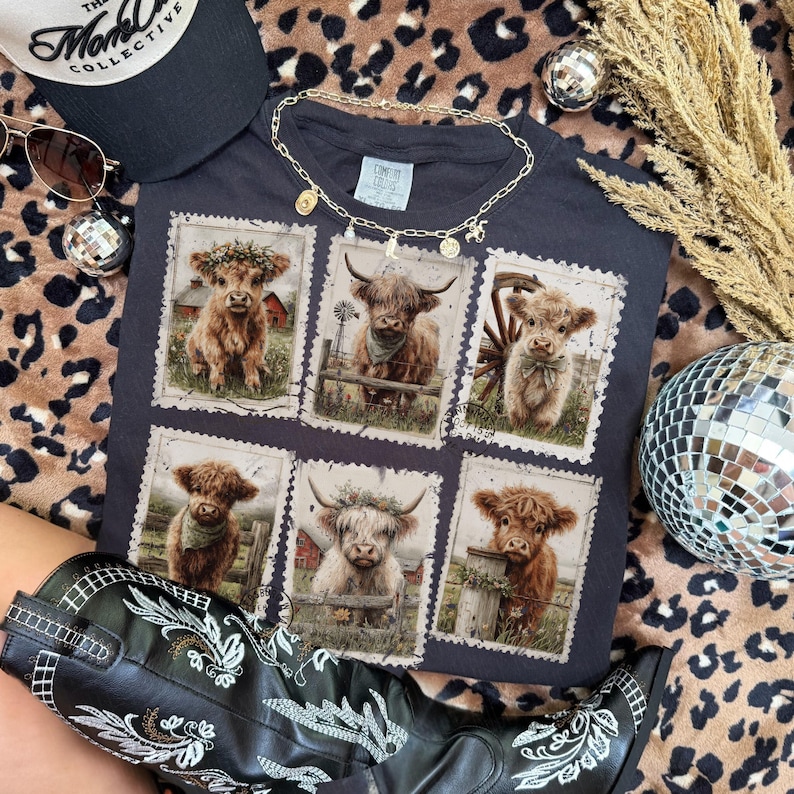 May include: Dark gray t-shirt featuring six postage stamp-style images of Highland cows. The shirt is accessorized with a gold necklace, sunglasses, and a black baseball cap. A pair of black cowboy boots with white embroidery are also visible.