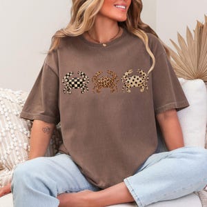 以下が含まれることがあります： 茶色のTシャツ。3匹のカニのデザインがあり、それぞれ異なるパターンです。白黒のチェッカーボード、ヒョウ柄、黒い水玉模様。Tシャツは半袖でゆったりとしたフィット感です。