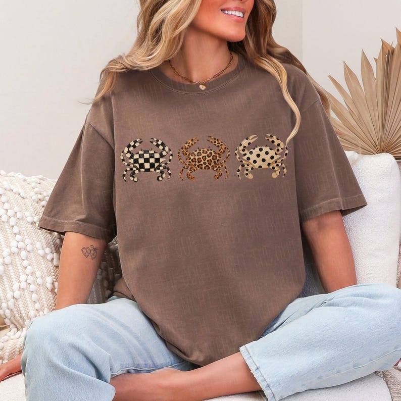 以下が含まれることがあります： 茶色のTシャツ。3匹のカニのデザインがあり、それぞれ異なるパターンです。白黒のチェッカーボード、ヒョウ柄、黒い水玉模様。Tシャツは半袖でゆったりとしたフィット感です。