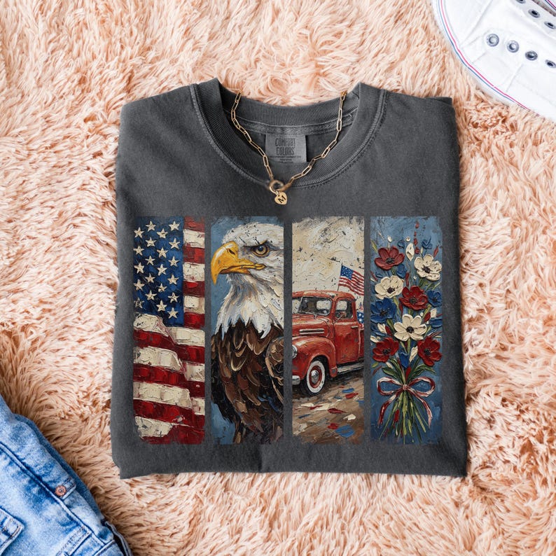 Puede incluir: Camiseta gris oscuro con un dise&ntilde;o patri&oacute;tico. El dise&ntilde;o incluye la bandera estadounidense, un &aacute;guila calva, una camioneta roja con una bandera y un ramo de flores rojas, blancas y azules. Se ve un collar dorado.