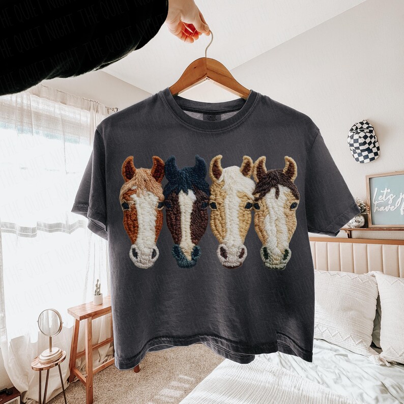 Peut inclure: T-shirt gris fonc&eacute; orn&eacute; de quatre t&ecirc;tes de chevaux brod&eacute;es en marron, blanc et bleu. Les t&ecirc;tes de chevaux sont dispos&eacute;es en rang&eacute;e sur le devant. Le t-shirt est suspendu &agrave; un cintre en bois.