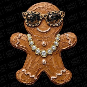 May include: A brown gingerbread person figure with a textured, impasto-style paint finish. The figure wears leopard-print sunglasses and a gold-toned necklace featuring clear, faceted stones. White icing-style wavy lines accent the limbs.