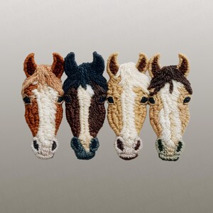Peut inclure: Quatre &eacute;cussons brod&eacute;s en forme de t&ecirc;te de cheval de diff&eacute;rentes couleurs : beige, bleu fonc&eacute;, marron et beige clair. Chaque &eacute;cusson pr&eacute;sente des coutures d&eacute;taill&eacute;es, avec des accents blancs et marrons, et un fond neutre.