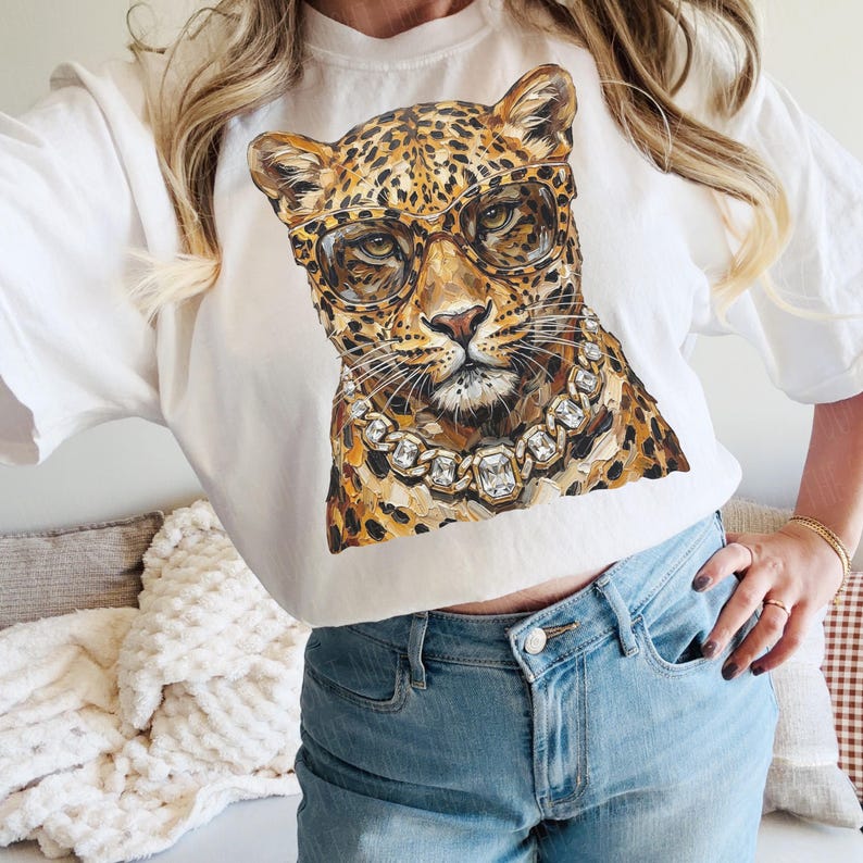 Puede incluir: Camiseta blanca de cuello redondo con un leopardo con gafas y una cadena de diamantes. El leopardo tiene un patr&oacute;n de manchas marrones y beige. Las gafas tienen montura dorada. La cadena tiene gemas cuadradas grandes.
