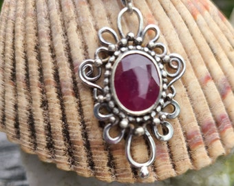 May include: A silver pendant with a dark pink gemstone set in a filigree design.