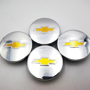 Peut inclure: Quatre enjoliveurs circulaires chromés, chacun orné d'un logo Chevrolet jaune et argenté. Les enjoliveurs ont une surface réfléchissante, ce qui leur donne un aspect brillant. Le logo jaune est un élément de design clé, sur fond argenté.