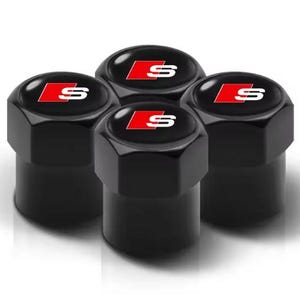 May include: Set of four black valve stem caps. Each cap features a glossy black finish with a red and white "S" logo. The caps have a hexagonal shape and are designed for automotive use.