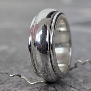 May include: A close-up of a silver ring with a textured, ridged design. The ring has a polished, reflective surface. The brand name "KSliverarts" is visible on the ring.
