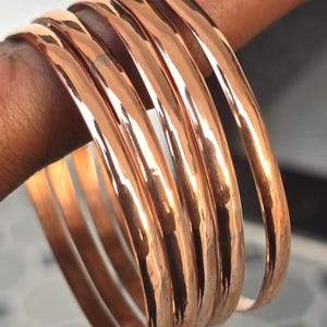 Peut inclure: Un ensemble de bracelets de couleur cuivre. Le métal poli reflète la lumière, créant un aspect chaleureux et brillant. Les bracelets ronds semblent être de taille uniforme, suggérant un ensemble de bijoux.