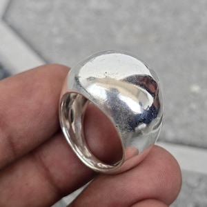 以下が含まれることがあります： 丸みを帯びたドーム型のトップが付いた、磨かれたシルバーカラーのリング。 リングは滑らかで反射する表面を持ち、バンドは太くてしっかりしています。 このリングは、普段使いや特別な機会に適した、ステートメントピースです。