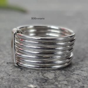 Op de afbeelding: Een zilveren ring met een multi-band ontwerp. De ring heeft meerdere parallelle banden van gepolijst metaal, waardoor een gelaagd effect ontstaat. De ring is een eenvoudig, maar elegant sieraad.