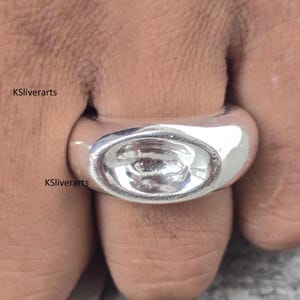 Può includere: Primo piano di un anello d'argento con castone ovale. L'anello è indossato su un dito e il castone sembra vuoto. L'anello ha una superficie lucida e riflettente. Il testo "KSliverarts" è visibile sull'immagine.
