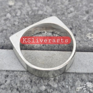 Op de afbeelding: Een zilveren ring met een geometrisch ontwerp. De ring heeft een platte band en een vierkante bovenkant met een puntige rand. De tekst "KSliverarts" is zichtbaar op de ring.