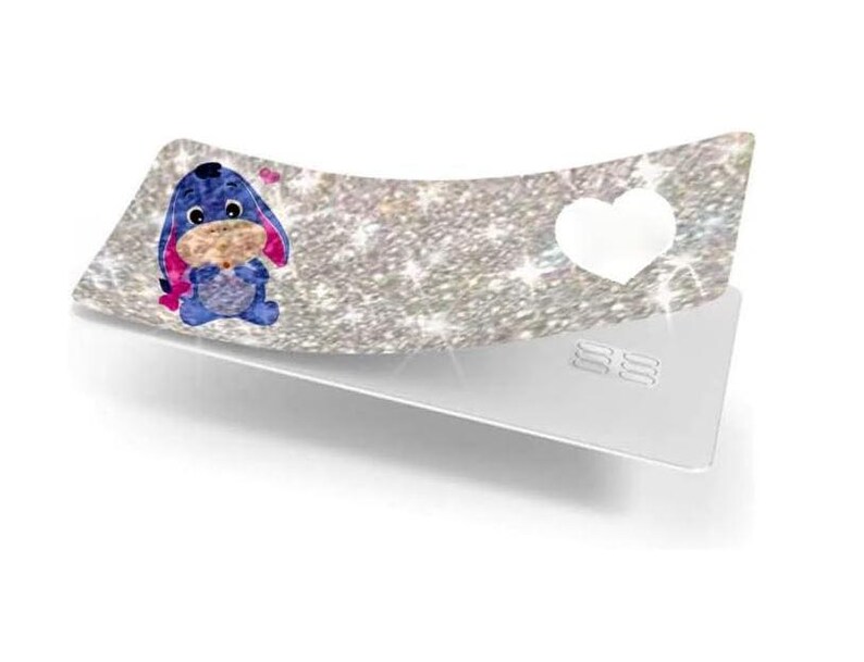 May include: A decorative, curved tray with a glittery silver surface. The tray features a cartoon image of Eeyore, a white heart, and a silver base. The Eeyore image is blue, pink, and tan.