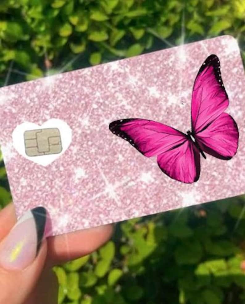 Puede incluir: Una tarjeta rosa brillante con un dise&ntilde;o de mariposa rosa brillante. La tarjeta tiene un recorte en forma de coraz&oacute;n blanco con un chip. La mariposa tiene detalles negros en sus alas.