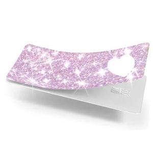 May include: A light purple, glittery card cover with a heart-shaped cutout, resting on a silver credit card. The cover has a sparkling texture and a curved shape, creating a decorative effect.