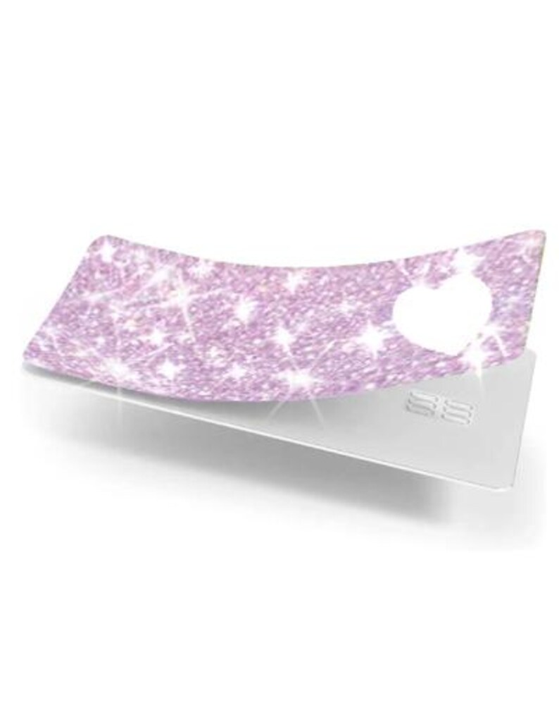 May include: A light purple, glittery card cover with a heart-shaped cutout, resting on a silver credit card. The cover has a sparkling texture and a curved shape, creating a decorative effect.