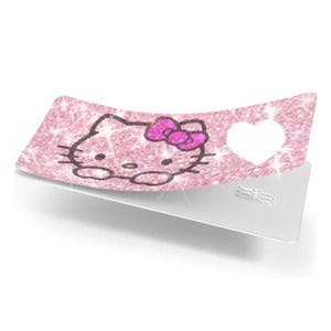 May include: A pink glittery card with a Hello Kitty design and a white heart cutout. The Hello Kitty graphic has a pink bow and is outlined in black. The card is on a white surface.
