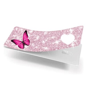 Puede incluir: Una tarjeta decorativa con un dise&ntilde;o de purpurina rosa y una mariposa rosa brillante en el lado izquierdo. Una forma de coraz&oacute;n blanco est&aacute; recortada en el lado derecho. La tarjeta est&aacute; colocada sobre una tarjeta plateada.