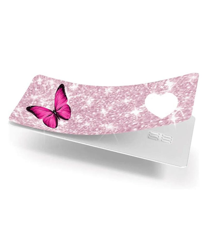 Puede incluir: Una tarjeta decorativa con un dise&ntilde;o de purpurina rosa y una mariposa rosa brillante en el lado izquierdo. Una forma de coraz&oacute;n blanco est&aacute; recortada en el lado derecho. La tarjeta est&aacute; colocada sobre una tarjeta plateada.