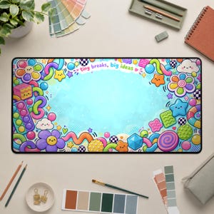 May include: A rectangular desk mat featuring a light blue centre surrounded by a colourful border of cartoon shapes including flowers, stars, clouds, and geometric forms. The text "tiny breaks, big ideas" is printed in small letters at the top.