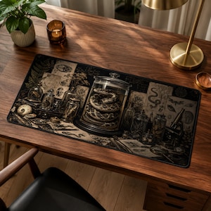 May include: A rectangular desk mat featuring a dark, vintage-style illustration of a coiled snake inside a glass jar, surrounded by various apothecary bottles, botanical sketches, a microscope, and an ammonite fossil on a dark background.