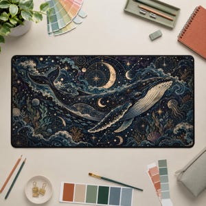 May include: A rectangular desk mat featuring a dark blue and gold celestial illustration of a whale swimming through a starry night sky filled with crescent moons, constellations, swirling clouds, and intricate geometric patterns.