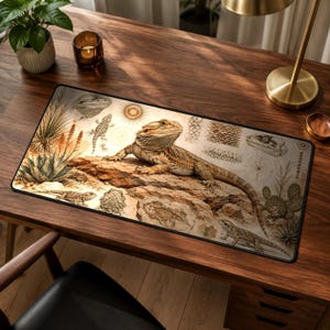 Könnte beinhalten: Eine rechteckige Schreibtischunterlage mit einer zentralen Illustration einer Bartagame auf einem Felsen, umgeben von kleineren Skizzen von Echsen, Wüstenpflanzen, Kakteen und Sonnenmotiven in Beige-, Braun- und Ockertönen mit schwarzem Rand.