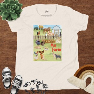 May include: A light-colored t-shirt featuring a colorful illustration of farm animals, including cows, chickens, and dogs, with the text "My Farm." The shirt has a crew neck and short sleeves.
