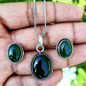 May include: A jewelry set featuring a dark green oval stone pendant necklace, matching earrings, and a ring. The stones are set in a silver-colored metal with a rope-like border. The necklace chain is also silver.