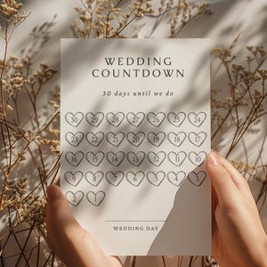 Könnte beinhalten: Eine cremefarbene Hochzeits-Countdown-Karte mit dem Text "WEDDING COUNTDOWN" und "30 Tage bis wir uns trauen". Die Karte zeigt 30 herzförmige Kästchen mit den Nummern 1-30. Die Worte "WEDDING DAY" stehen unten.