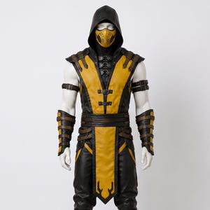May include: A yellow and black hooded costume featuring a matching yellow face mask, shoulder armor, arm guards, and a belt with multiple straps and buckles. The outfit includes a sleeveless tunic with a long front panel and fitted trousers.
