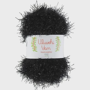 Puede incluir: Una madeja de hilo negro Ululuwehi con purpurina. El hilo está envuelto con una etiqueta blanca que tiene las palabras "Ululuwehi Yarn" en escritura roja y amarilla. La etiqueta también dice "black w/glitter".