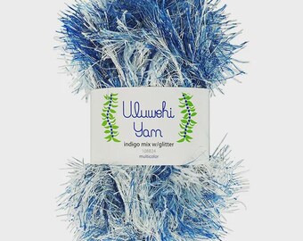 May include: A skein of Ulwehi Yarn in indigo mix with glitter. The yarn is a mix of blue and white fibers, creating a fluffy, textured appearance. The label reads "Ulwehi Yarn" and includes the product details.