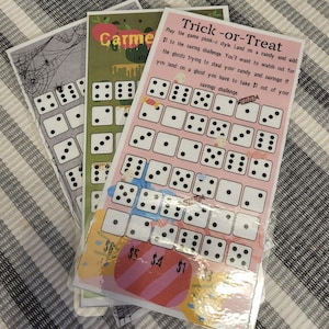 May include: Three colorful game cards with dice patterns. One card has a Halloween theme with spiders and webs. Another has a green background with the text "Carme Lan". The third card is pink and has the text "Trick-or-Treat".