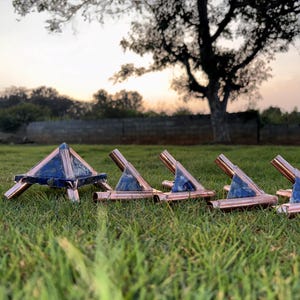 May include: A collection of copper and blue stone pyramids and stands arranged on green grass. The pyramid has a square base and is supported by copper legs. The stands have a copper frame with a blue stone insert.