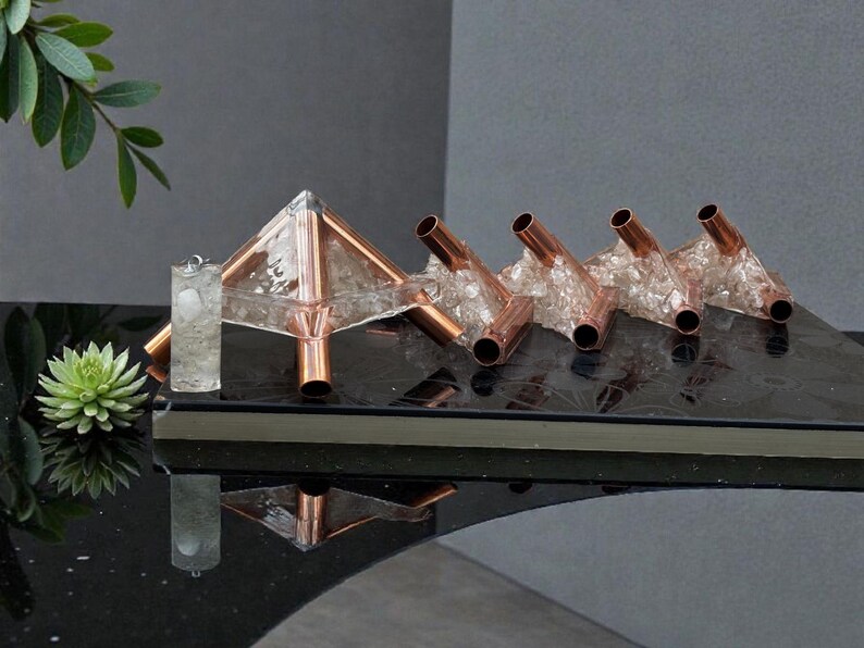 May include: A collection of copper and crystal decorative objects. The centerpiece is a pyramid shape with copper tubing and clear crystals. Adjacent are four copper tubes with crystal accents. A clear, cylindrical object is also present.