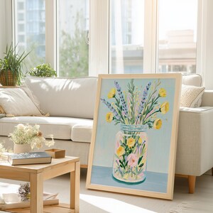May include: A framed art print featuring a colorful floral arrangement in a mason jar. The artwork showcases yellow, purple, and pink flowers against a light blue background. The frame is made of light-colored wood, adding a natural touch to the piece.