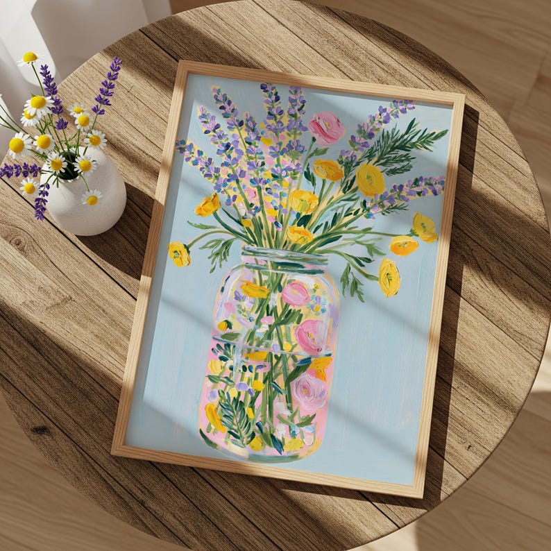 May include: A framed floral art print featuring a vibrant bouquet of lavender, yellow, and pink flowers in a mason jar against a light blue background. The artwork is displayed on a round wooden table, with a small vase of flowers nearby.