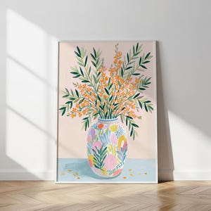 May include: A framed art print featuring a colorful vase filled with orange flowers and green foliage. The vase has a patterned design with pink, yellow, and blue shapes. The background is a light pink color, and the artwork is displayed on a light blue surface.