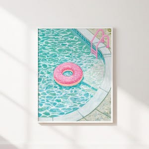 Può includere: Una stampa artistica incorniciata che raffigura una piscina color turchese con acqua increspata, un salvagente rosa brillante a forma di ciambella e una scaletta da piscina in metallo rosa abbinata sul bordo curvo in cemento bianco.