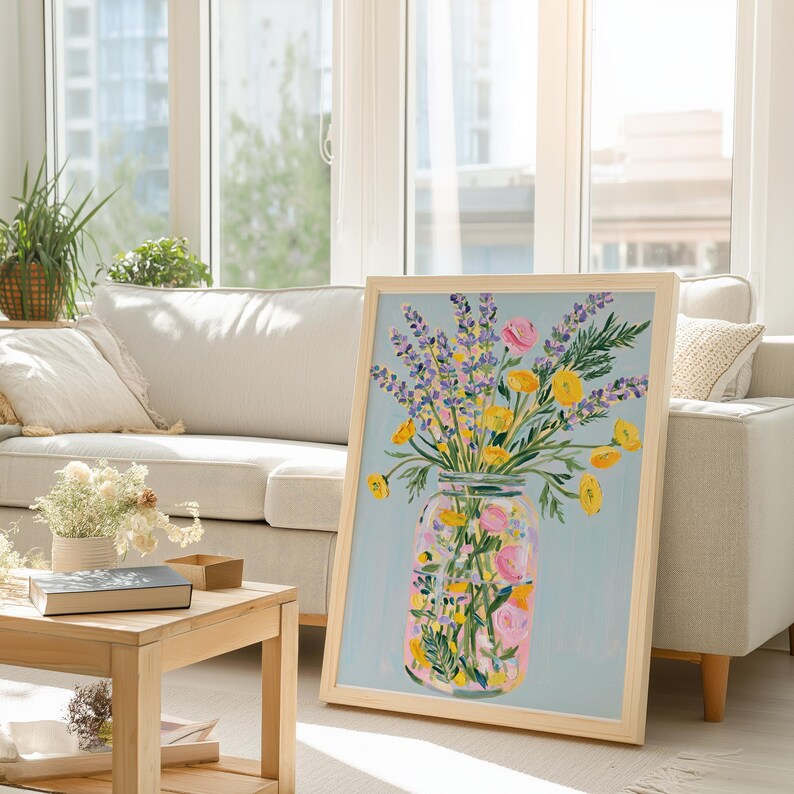 May include: A framed art print featuring a colorful floral arrangement in a mason jar. The artwork showcases yellow, pink, and purple flowers against a light blue background. The frame is made of light-colored wood.