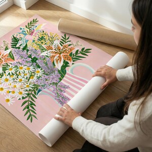 Pu&ograve; includere: Una stampa artistica floreale con un bouquet di gigli, margherite e lavanda in una brocca a righe rosa e bianche. La stampa &egrave; arrotolata con un rotolo di carta bianca.
