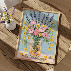 May include: A framed floral painting featuring a mason jar filled with pink roses, yellow flowers, and purple lavender. The background is light blue with yellow dots. The painting is on a wooden table.