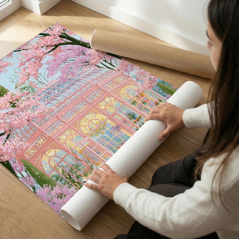 May include: A rolled-up art print featuring a pink greenhouse with intricate architectural details, surrounded by blooming cherry blossom trees. The print is on a wooden floor, with a second rolled print in the background.
