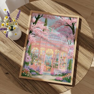 May include: A framed art print depicts a pink greenhouse surrounded by blooming cherry blossom trees. The artwork features a detailed illustration of the glass structure, with flowers and plants in the foreground. The print is set on a wooden table with a vase of flowers.