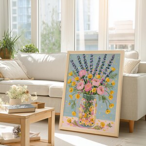 May include: A framed floral painting featuring a bouquet of pink roses, yellow buttercups, and purple lavender in a glass jar. The artwork has a light blue background with a pink and yellow patterned base, and is displayed in a light wood frame.