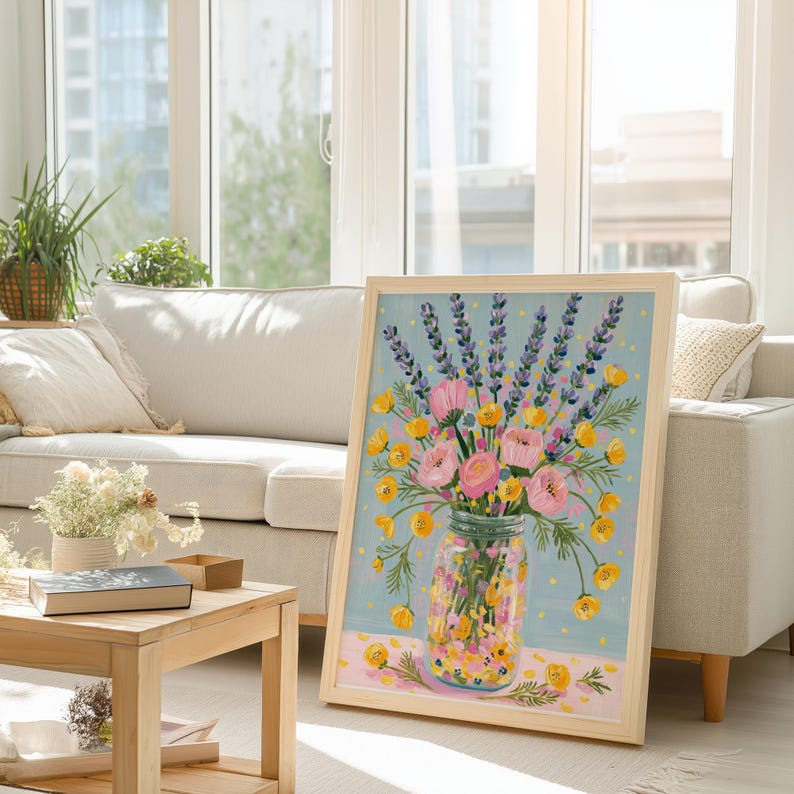 May include: A framed floral painting featuring a bouquet of pink roses, yellow buttercups, and purple lavender in a glass jar. The artwork has a light blue background with a pink and yellow patterned base, and is displayed in a light wood frame.